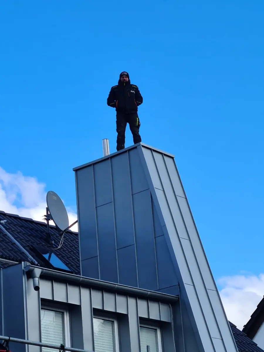 Ein Dachdecker von Hube steht auf einer neu mit Zink verkleideten Gaube, dahinter blauer Himmel